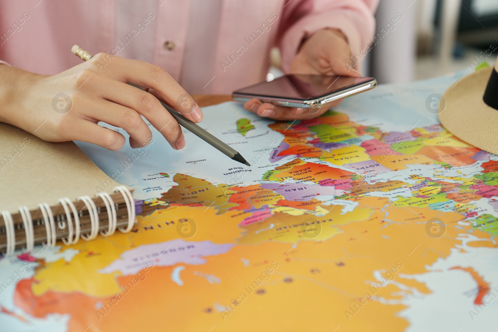 Photo of Woman with world map and smartphone planning trip at table, closeup]