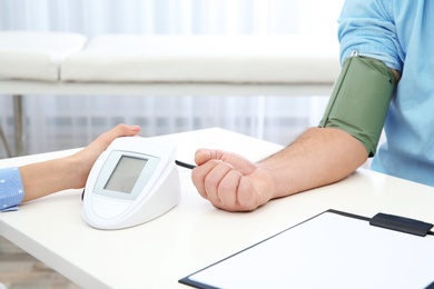 Doctor checking mature man's pulse with medical device in hospital, closeup