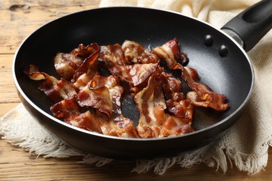 Photo of Delicious bacon slices in frying pan on wooden table, closeup