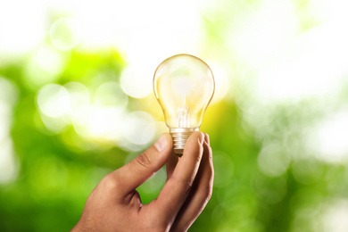 Image of Solar energy concept. Man holding glowing light bulb against green blurred background, closeup