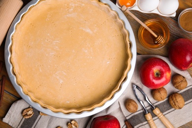 Photo of Raw dough and ingredients for traditional English apple pie on wooden table, flat lay