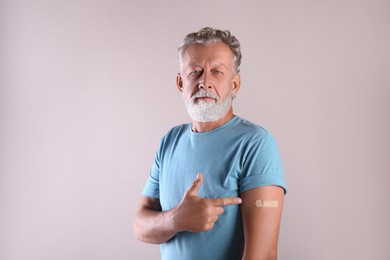Photo of Senior man pointing at arm with bandage after vaccination on beige background