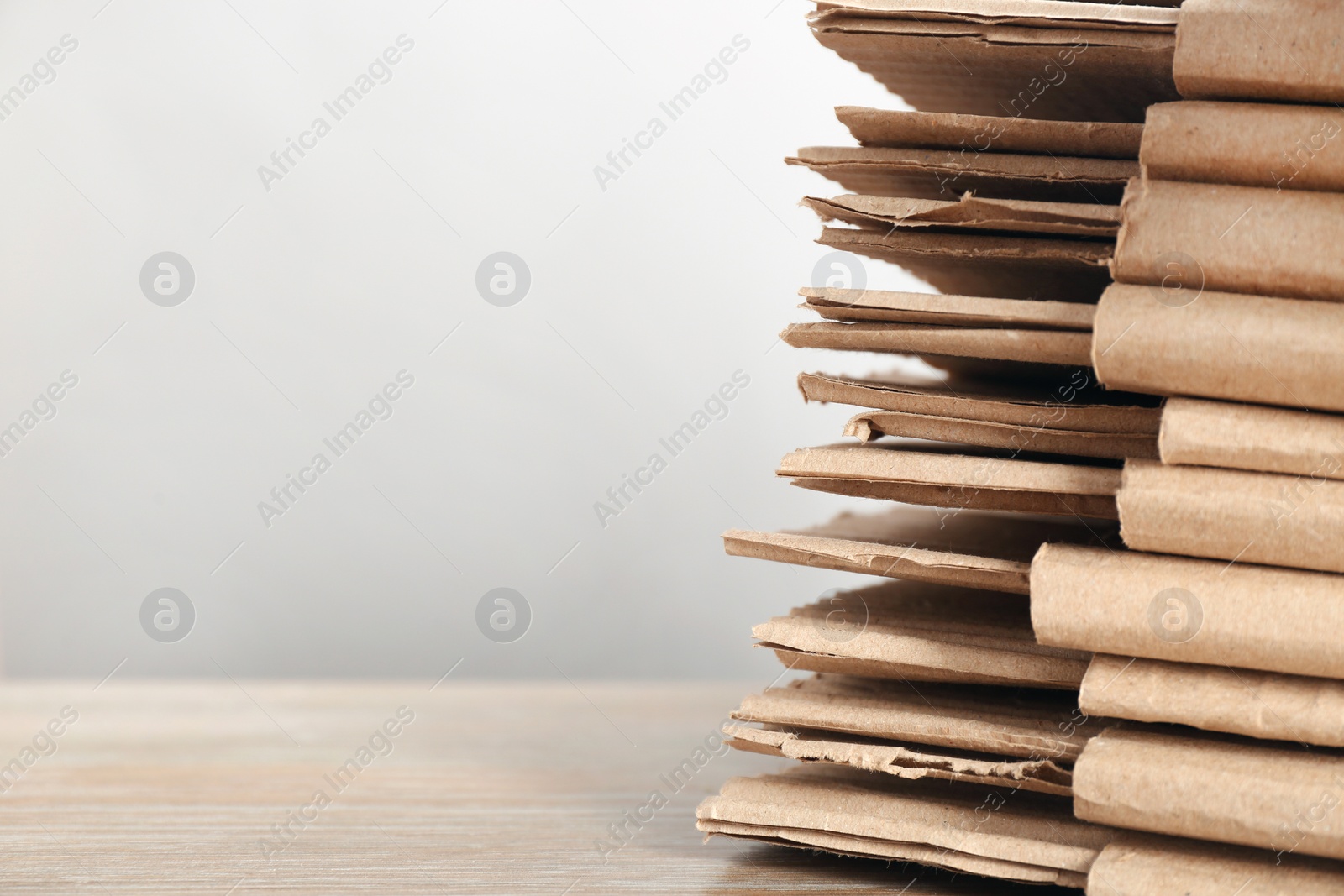 Photo of Cardboard pile on table against light background, space for text. Waste recycling concept