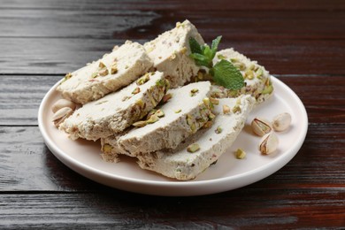 Photo of Pieces of tasty halva with pistachios and mint on wooden table, closeup