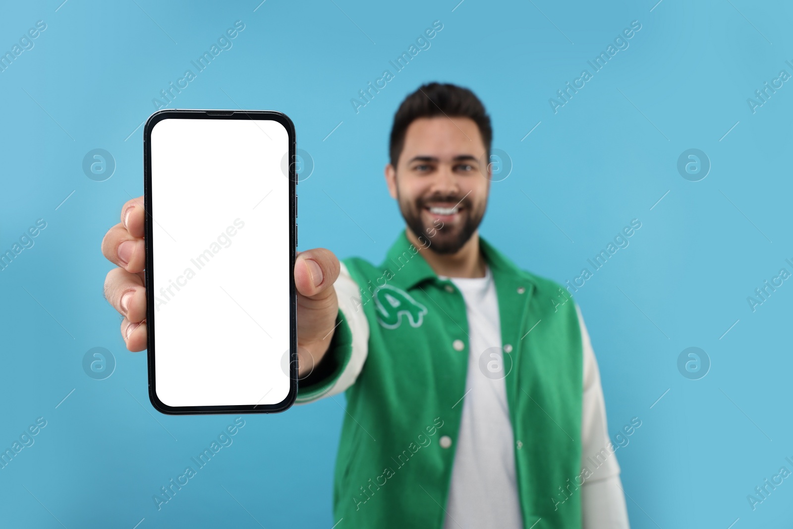 Photo of Young man showing smartphone in hand on light blue background, selective focus. Mockup for design