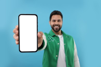 Photo of Young man showing smartphone in hand on light blue background, selective focus. Mockup for design