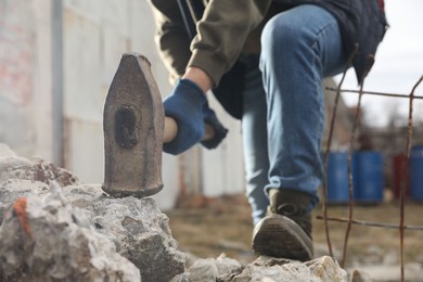 Photo of Man breaking stones with sledgehammer outdoors, closeup