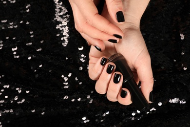 Photo of Woman with black manicure and nail polish bottle on dark background, top view. Space for text