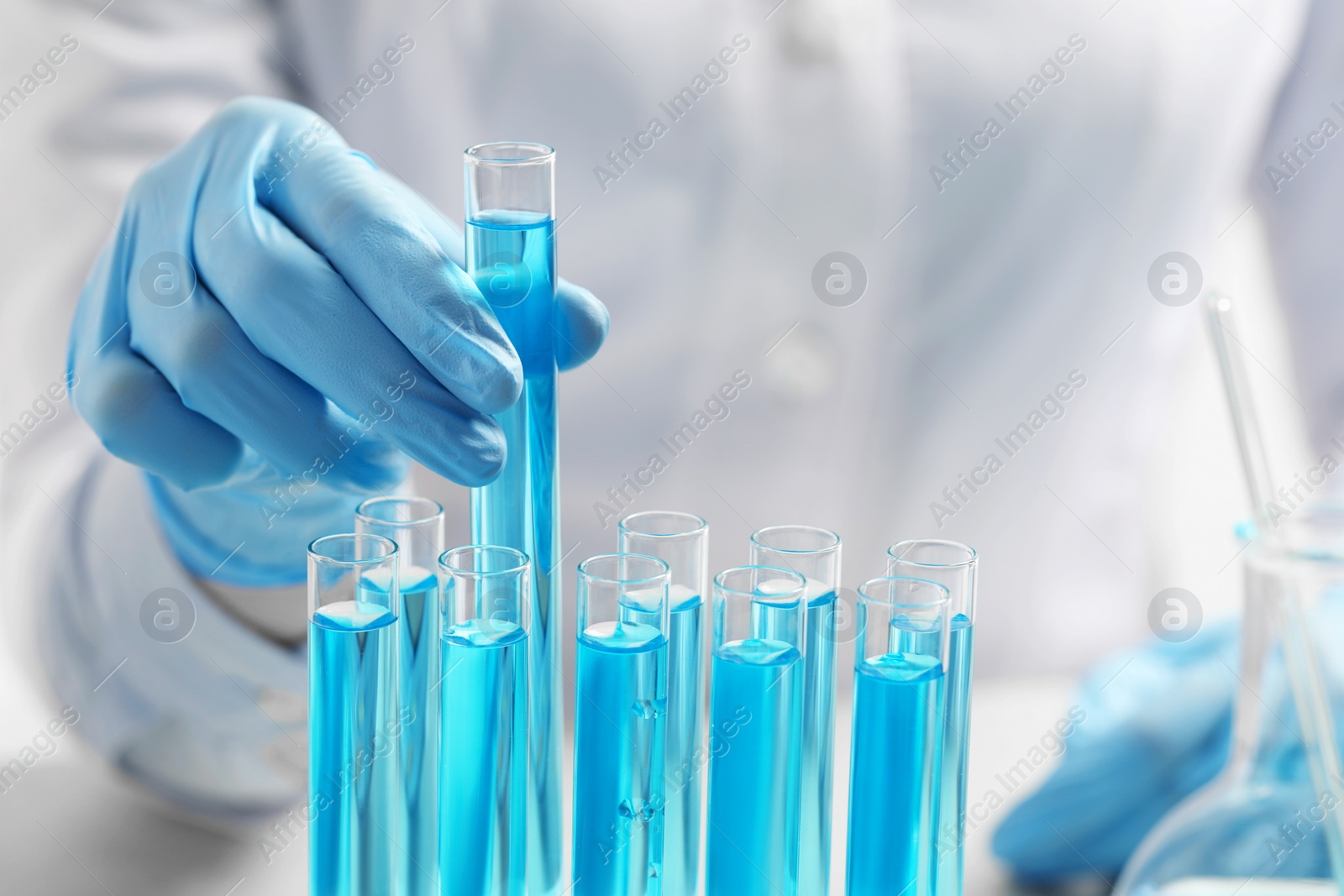 Photo of Scientist taking test tube with light blue liquid at table, closeup