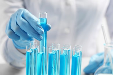 Photo of Scientist taking test tube with light blue liquid at table, closeup