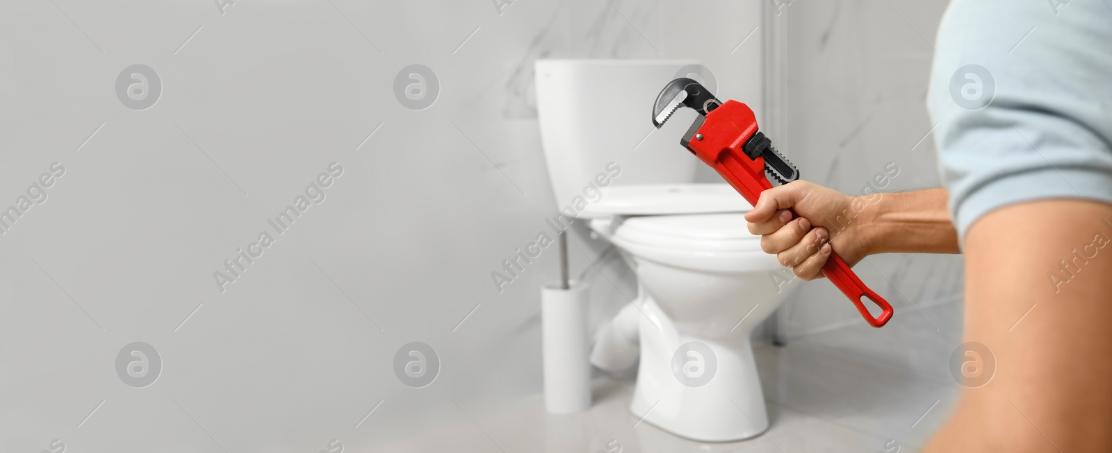 Image of Closeup view of professional plumber holding pipe wrench near toilet bowl in bathroom, space for text. Banner design