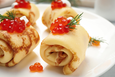 Delicious thin pancakes with red caviar on plate, closeup