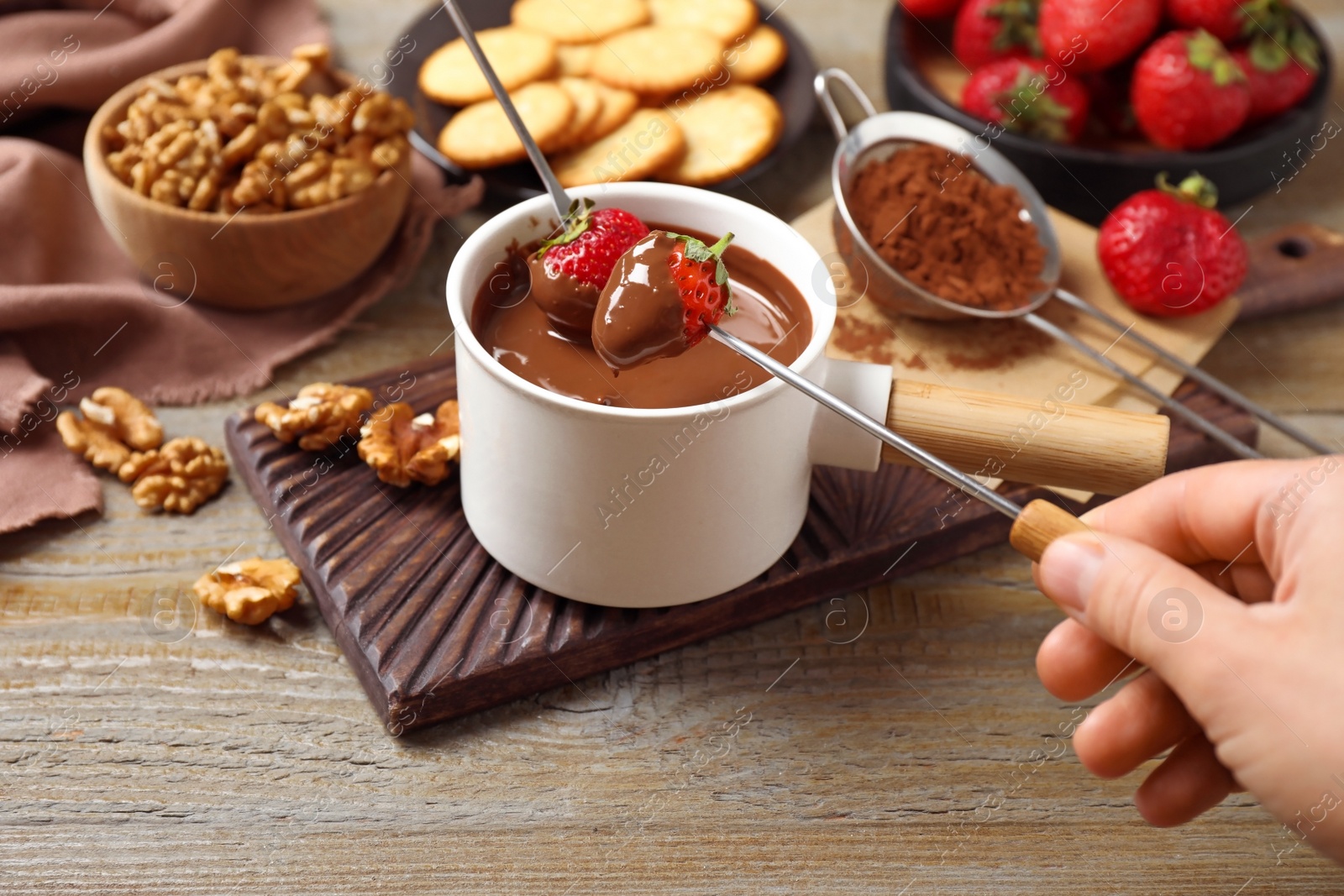 Photo of Woman dipping strawberry into fondue pot with milk chocolate at wooden table