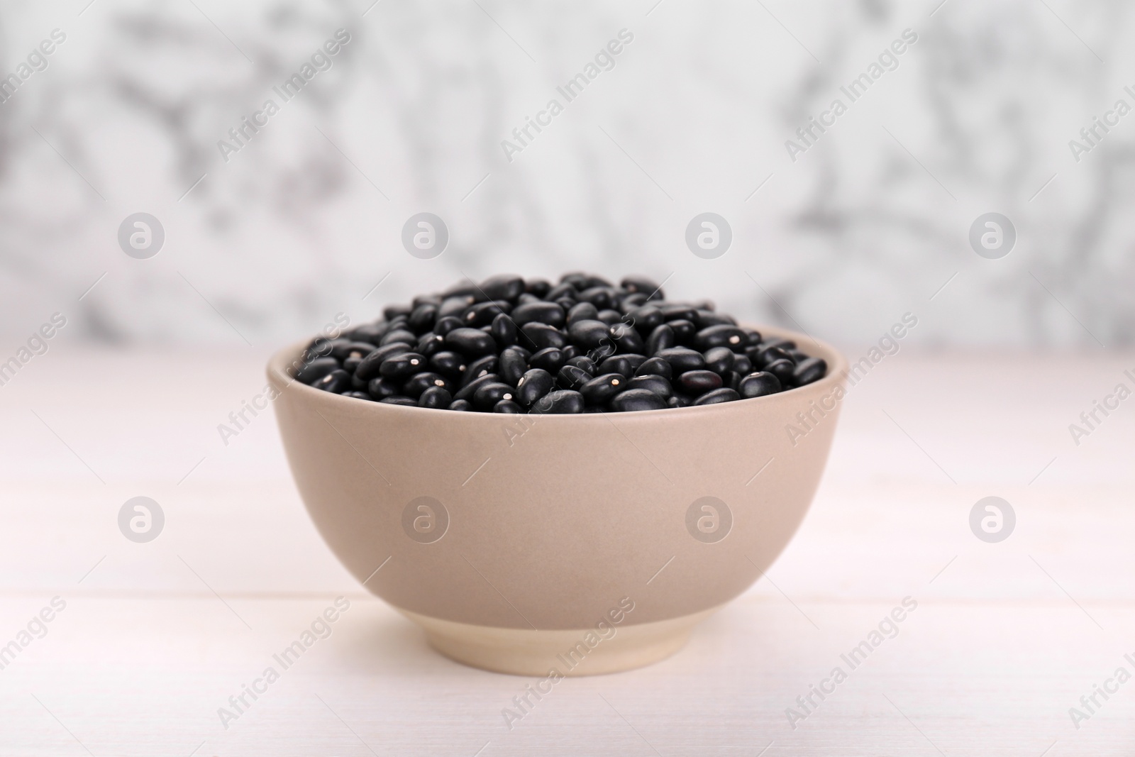 Photo of Bowl of raw black beans on white wooden table