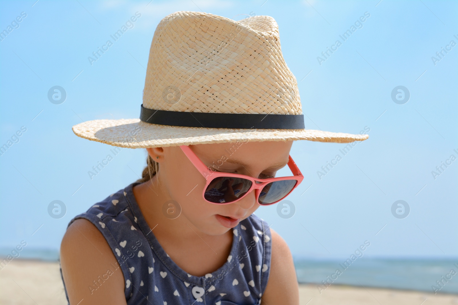 Photo of Little girl wearing sunglasses and hat at beach on sunny day