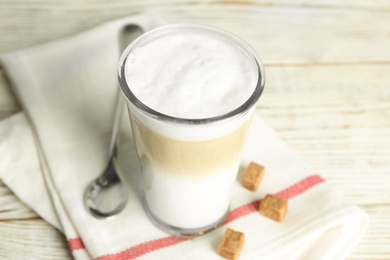 Delicious latte macchiato and sugar cubes on white wooden table