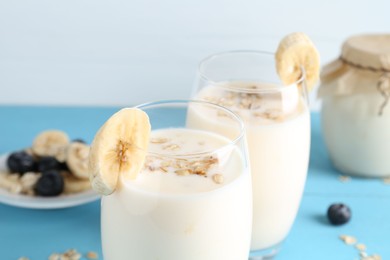 Tasty yogurt in glasses, oats, banana and blueberries on light blue table, closeup