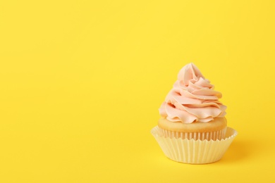 Tasty cupcake with cream on yellow background, space for text