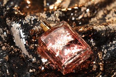 Photo of Luxury perfume in bottle on fabric with shiny sequins, closeup