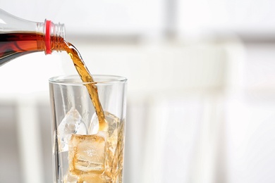 Pouring cola from bottle into glass on blurred background, closeup. Space for text
