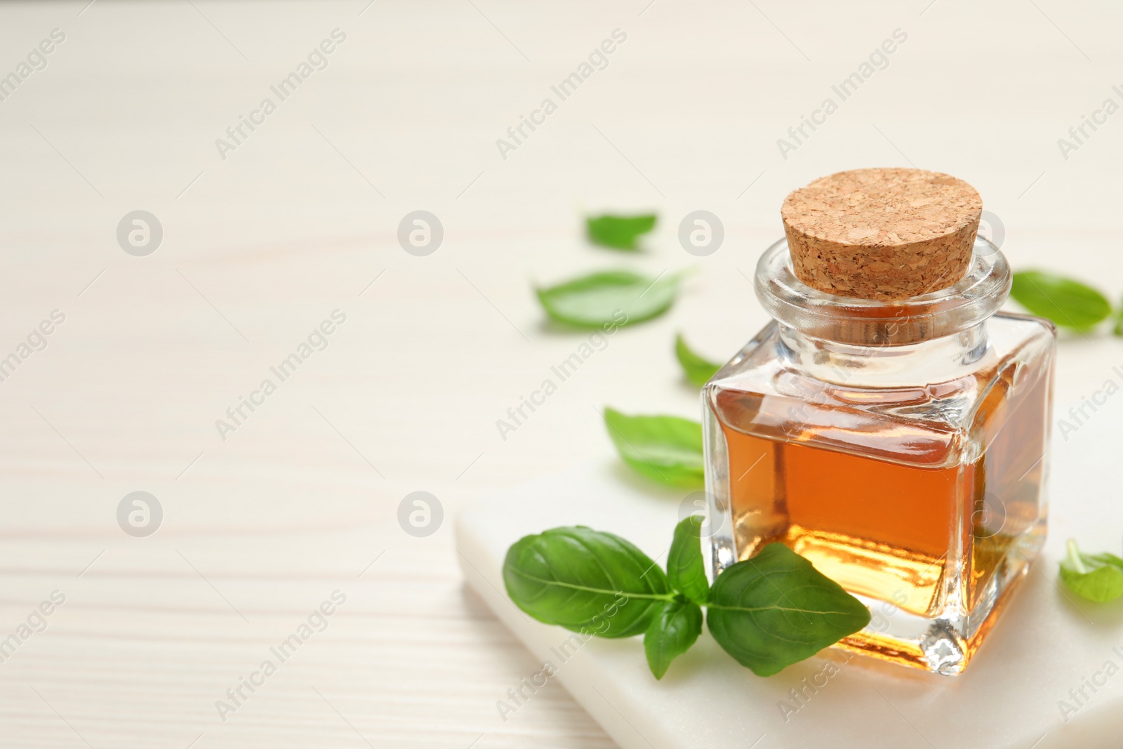 Photo of Bottle of essential basil oil and fresh leaves on white wooden table, space for text