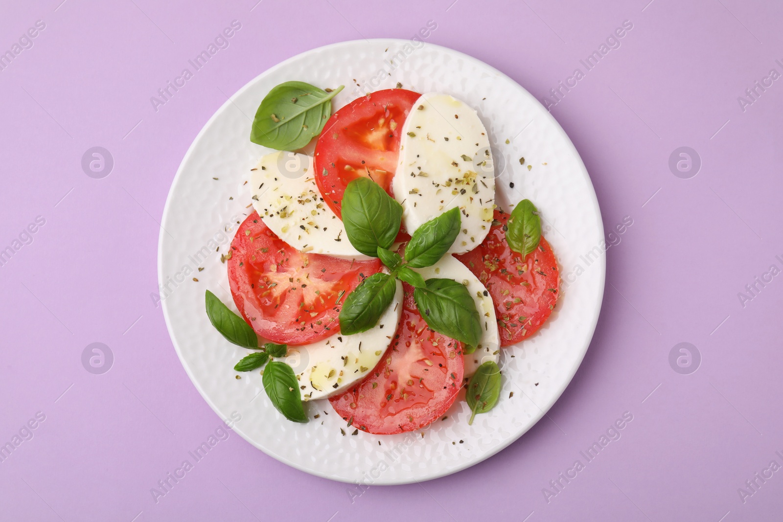 Photo of Plate of delicious Caprese salad with herbs on violet table, top view