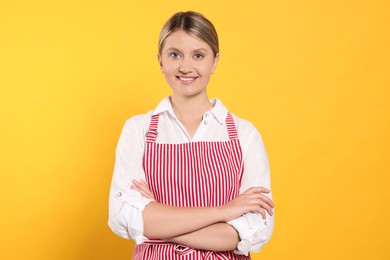 Photo of Beautiful young woman in clean striped apron on orange background
