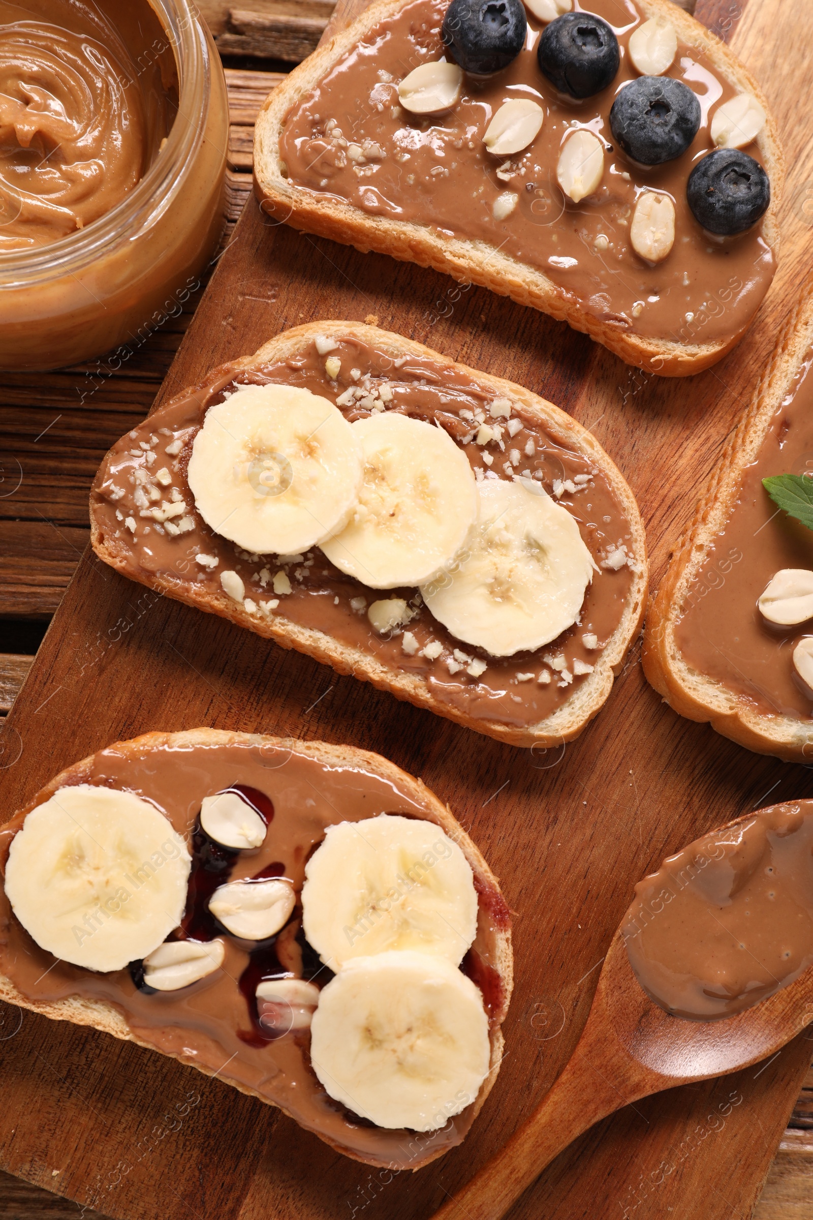 Photo of Toasts with tasty nut butter, banana slices, blueberries and peanuts on wooden table, flat lay