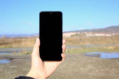 Woman holding mobile phone outdoors on sunny day, closeup. Space for text