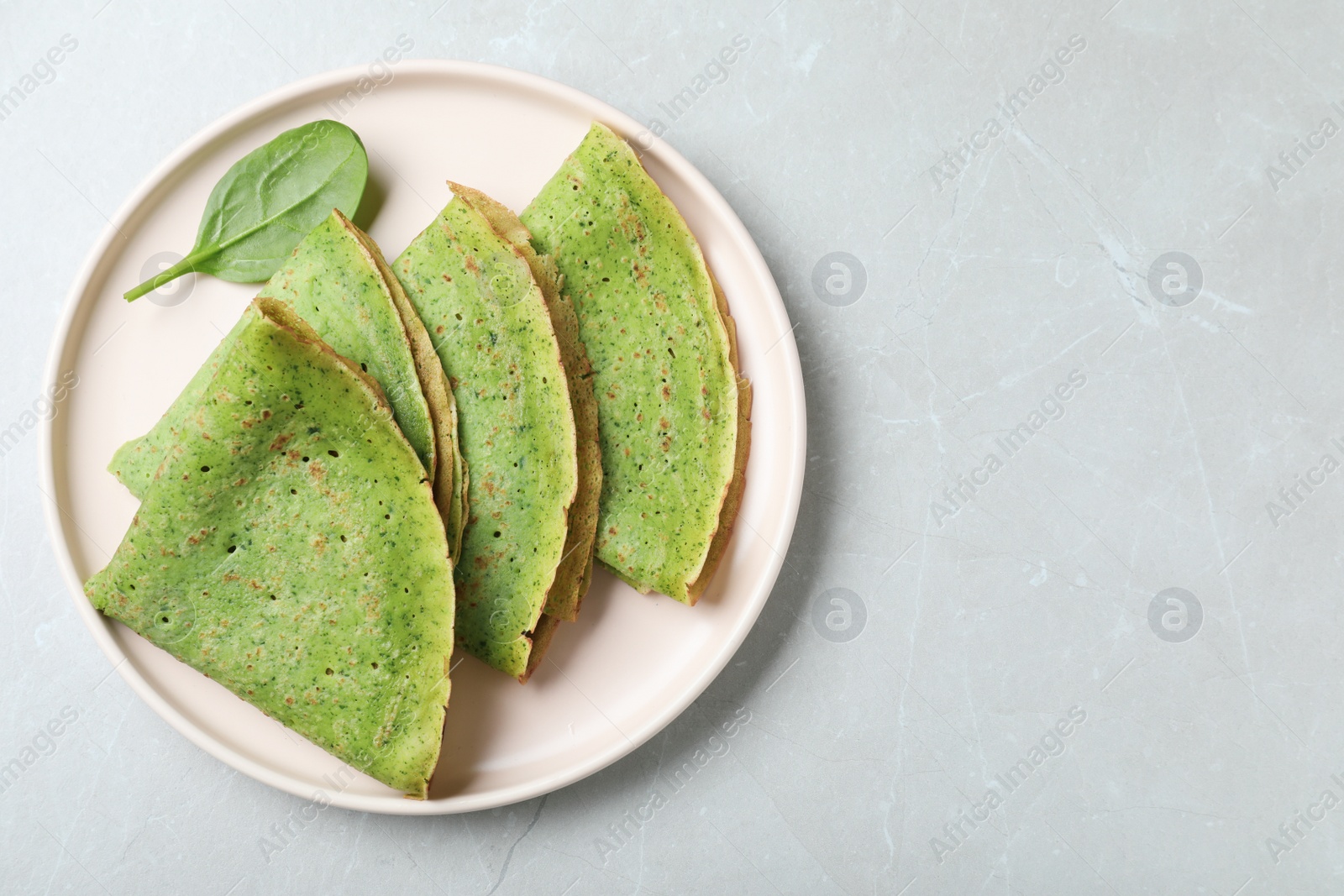 Photo of Tasty spinach crepes on light grey marble table, top view. Space for text