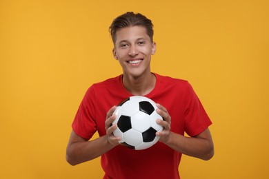 Photo of Happy sports fan with soccer ball on orange background