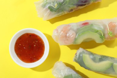 Delicious spring rolls and sauce on yellow background, flat lay