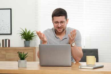 Man having video chat via laptop at wooden table at home
