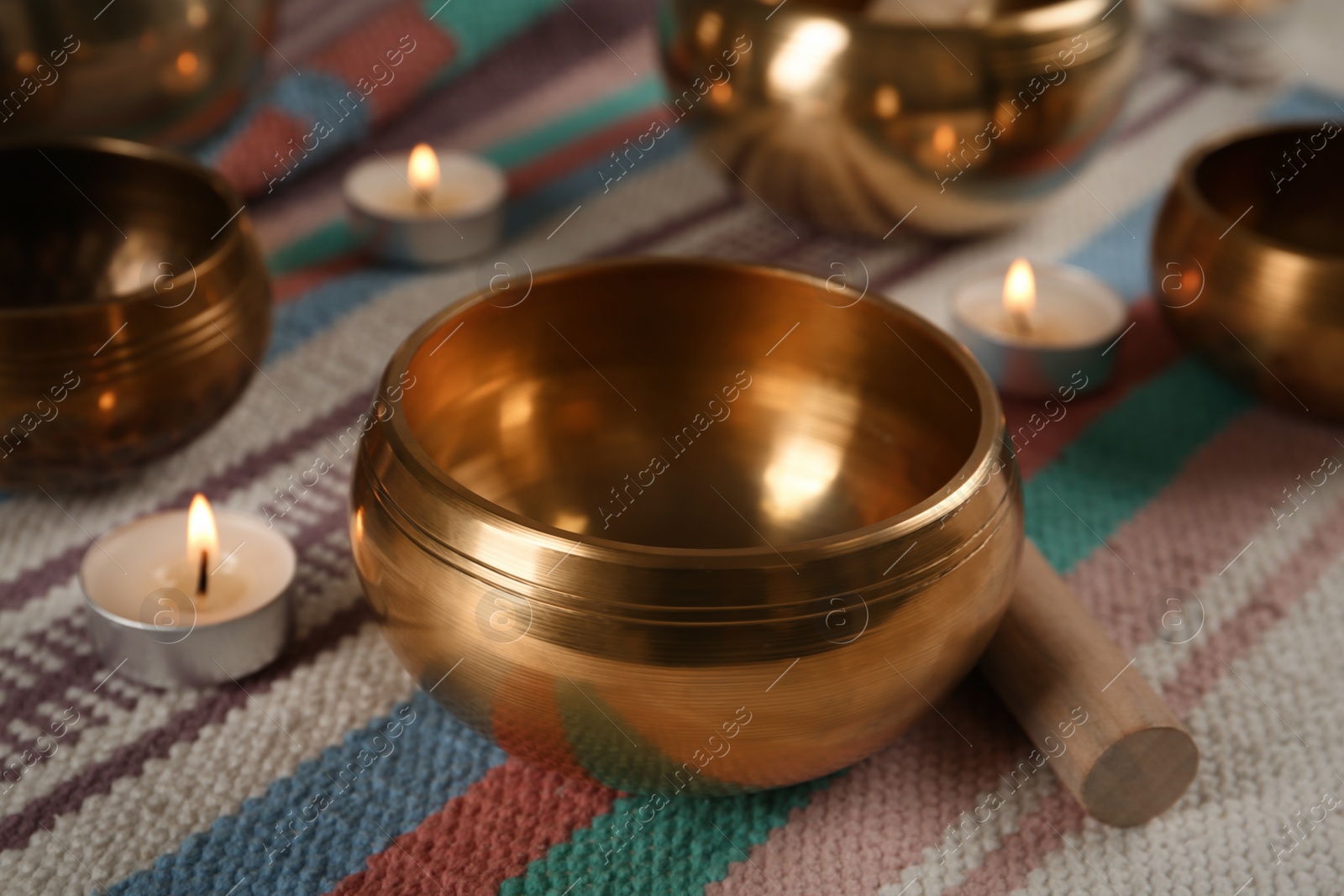 Photo of Tibetan singing bowls with mallet and burning candles on colorful fabric