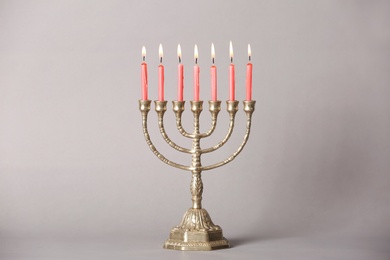 Golden menorah with burning candles on light grey background
