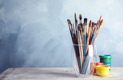 Photo of Glass with brushes and paint jars on table against color background. Space for text