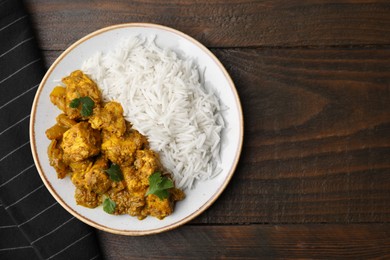 Photo of Delicious chicken curry with rice on wooden table, top view. Space for text