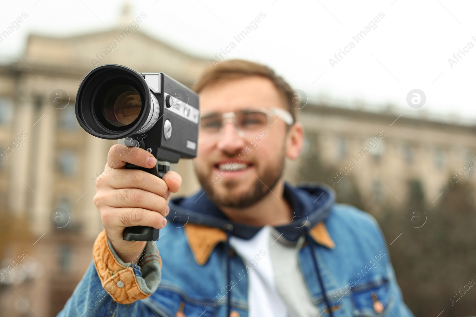 Photo of Young man with vintage video camera on city street, focus on lens