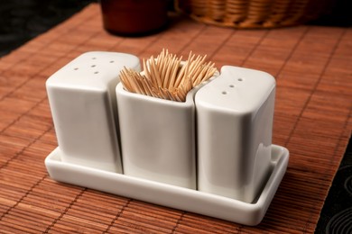 Photo of Holder with salt, pepper and toothpicks on bamboo mat, closeup
