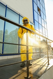 Photo of Person in hazmat suit with disinfectant sprayer cleaning metal railing on city street. Surface treatment during coronavirus pandemic