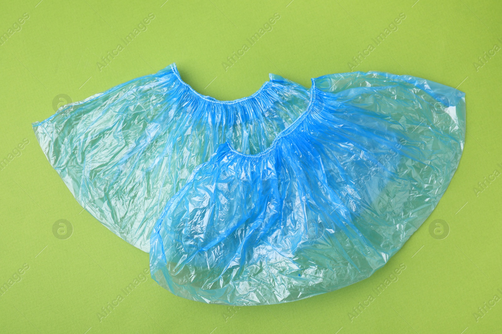 Photo of Pair of blue medical shoe covers on green background, top view