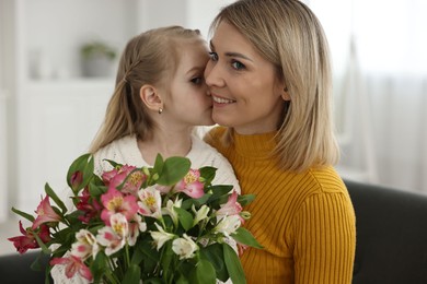 Photo of Little daughter kissing and congratulating her mom with bouquet of alstroemeria flowers at home. Happy Mother's Day