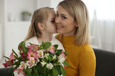 Little daughter kissing and congratulating her mom with bouquet of alstroemeria flowers at home. Happy Mother's Day