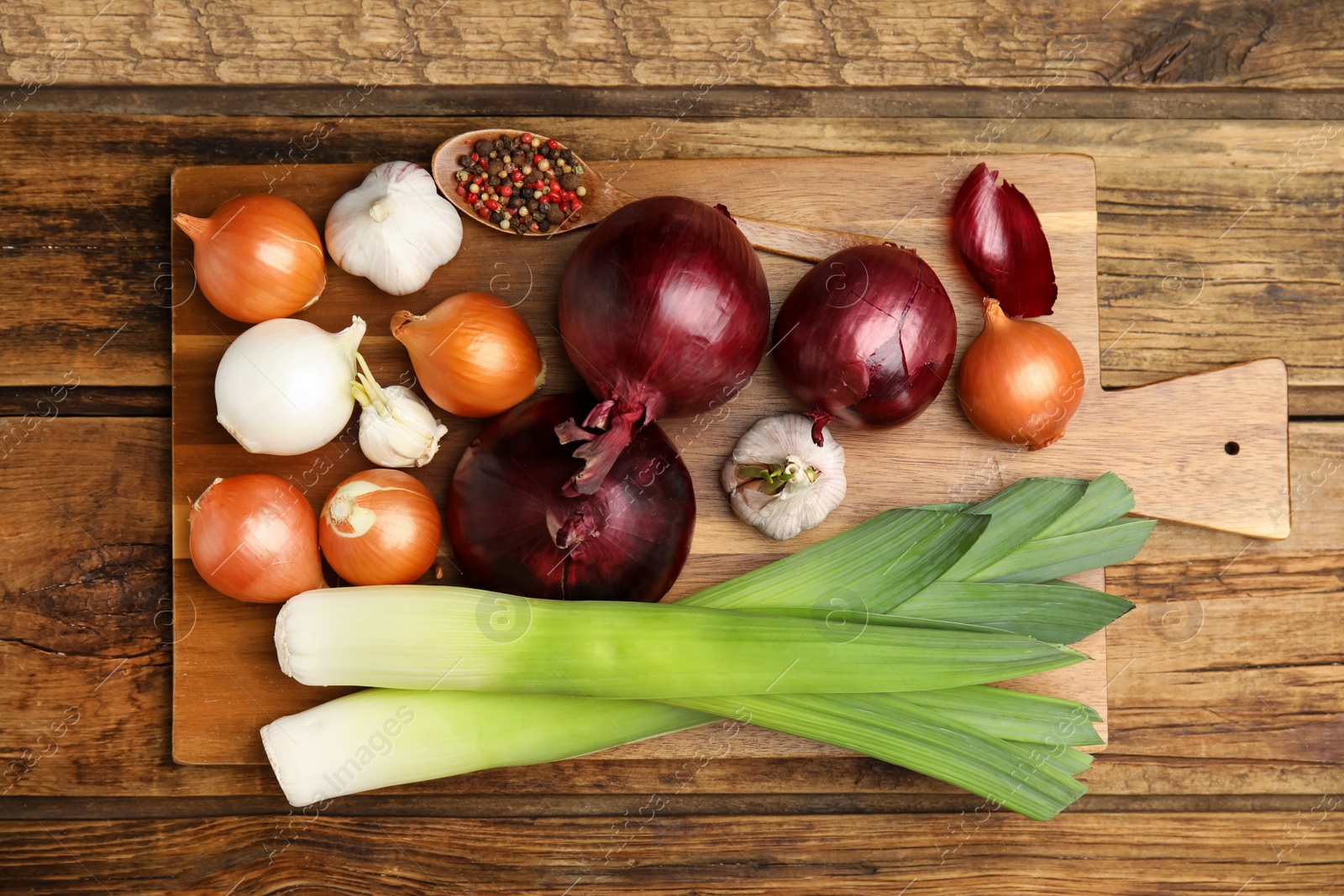 Photo of Fresh onion bulbs, leeks, garlic and peppers mix on wooden table, top view