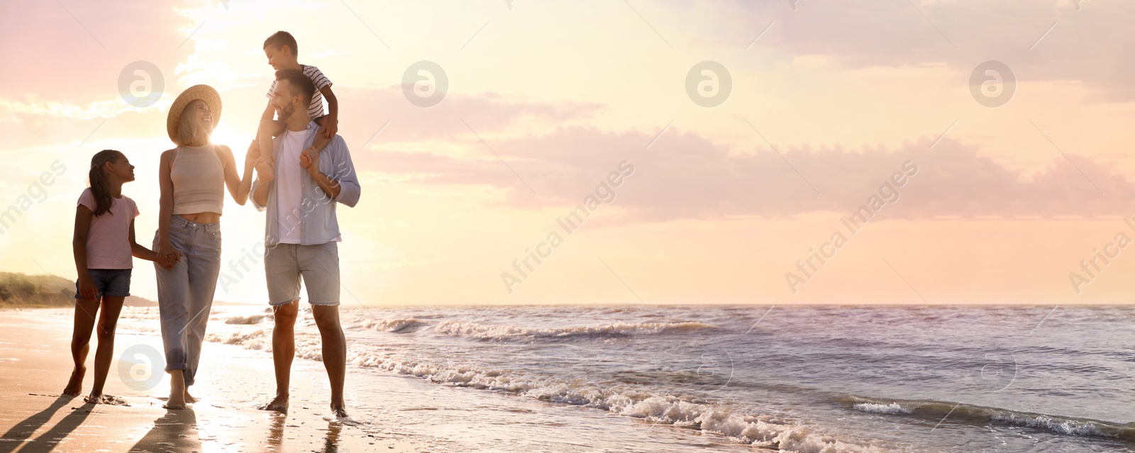 Image of Happy family walking on sandy beach near sea at sunset, space for text. Banner design