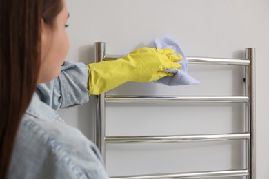 Woman cleaning heated towel rail with rag indoors, closeup