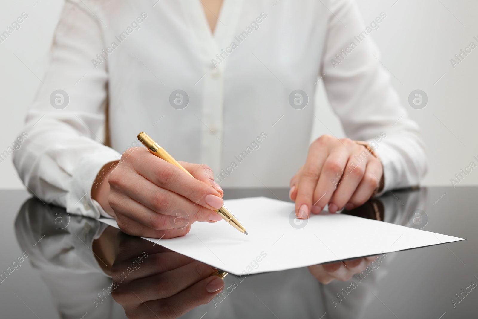 Photo of Woman writing on sheet of paper at glass table, closeup