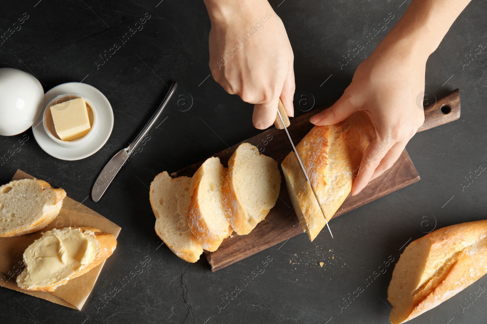 Photo of Woman cutting bread on black background, top view