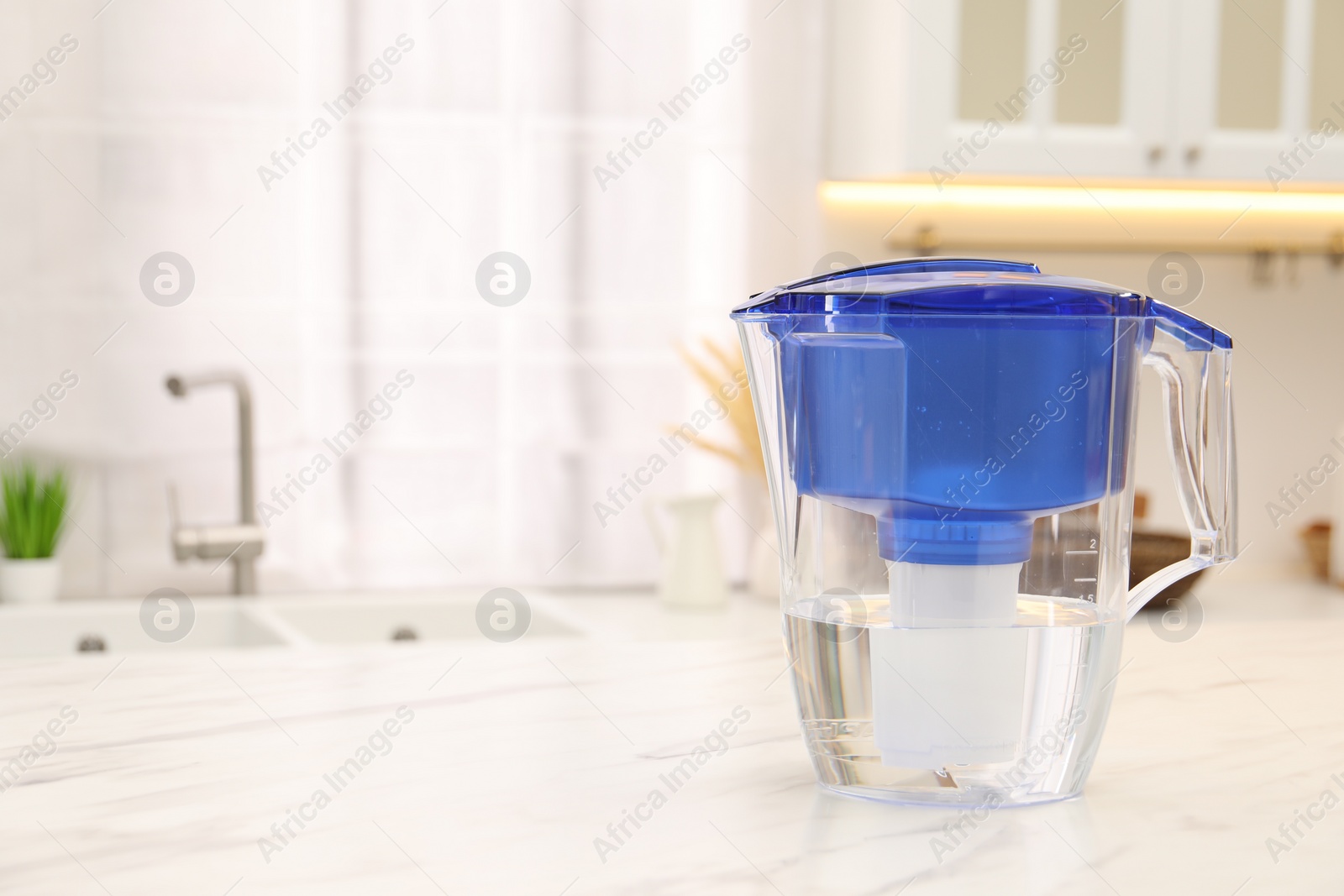 Photo of Water filter jug on white marble table in kitchen, space for text