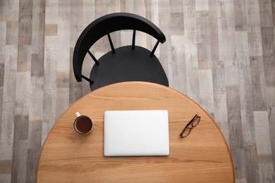 Round wooden table with cup of tea, computer tablet, and eyeglasses near black chair indoors, top view